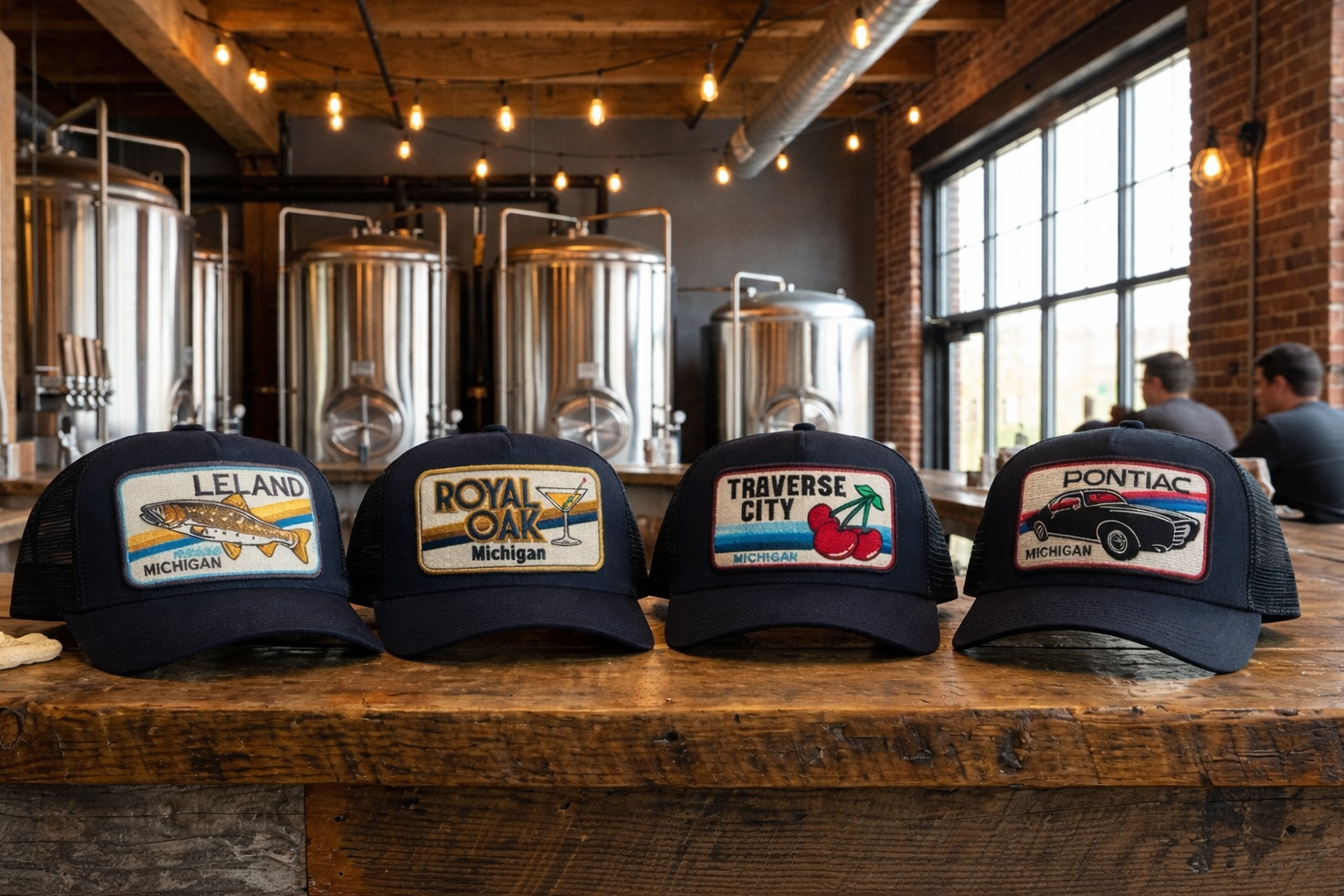 Four baseball caps with different city logos on a wooden table in a brewery setting.