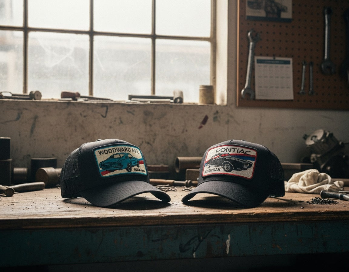 Two baseball caps with automotive-themed designs on a workshop counter.